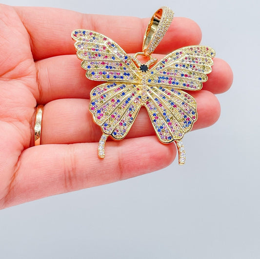 May include: Multicolored butterfly pendant. The pendant is gold-toned with a detailed butterfly design. The butterfly's wings are encrusted with small, sparkling stones in shades of pink, blue, yellow, and clear. The pendant features a detailed body and antennae. The pendant is a statement piece of jewelry.
