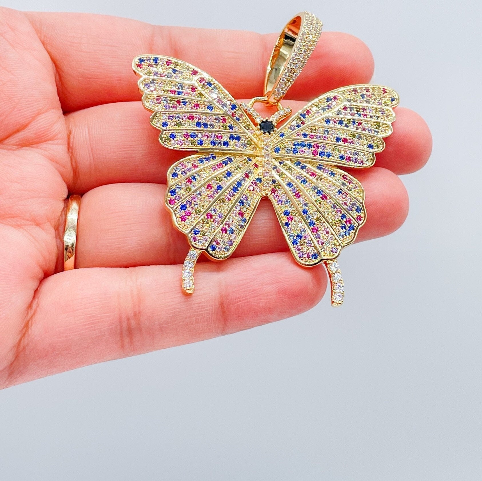 May include: Multicolored butterfly pendant.  The pendant is gold-toned with a detailed butterfly design.  The butterfly&#39;s wings are encrusted with small, sparkling stones in shades of pink, blue, yellow, and clear. The pendant features a detailed body and antennae.  The pendant is a statement piece of jewelry.