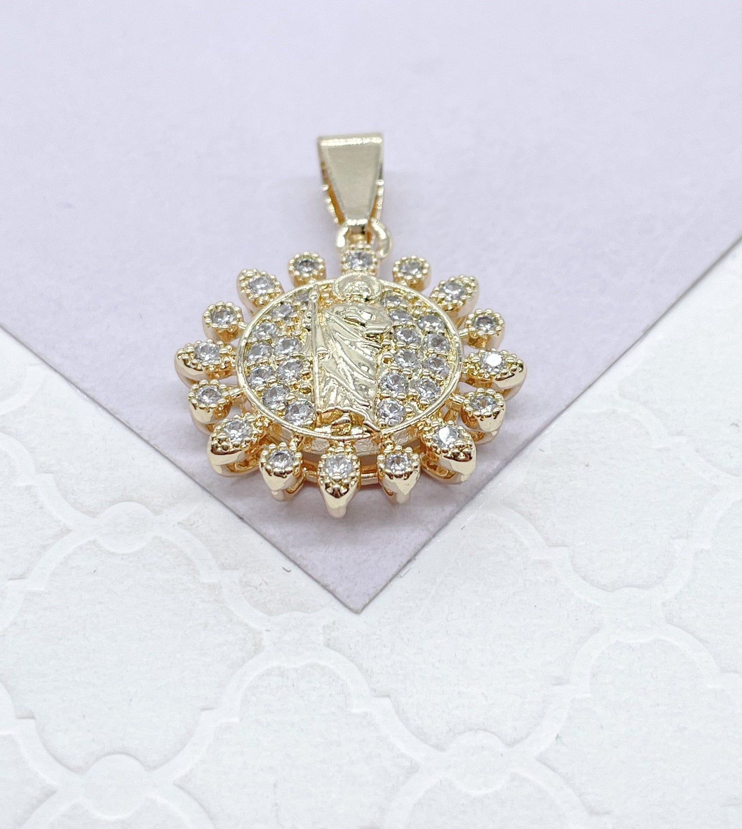 May include: Gold pendant with a clear crystal halo surrounding a religious figure. The pendant has a loop at the top for attaching to a chain.