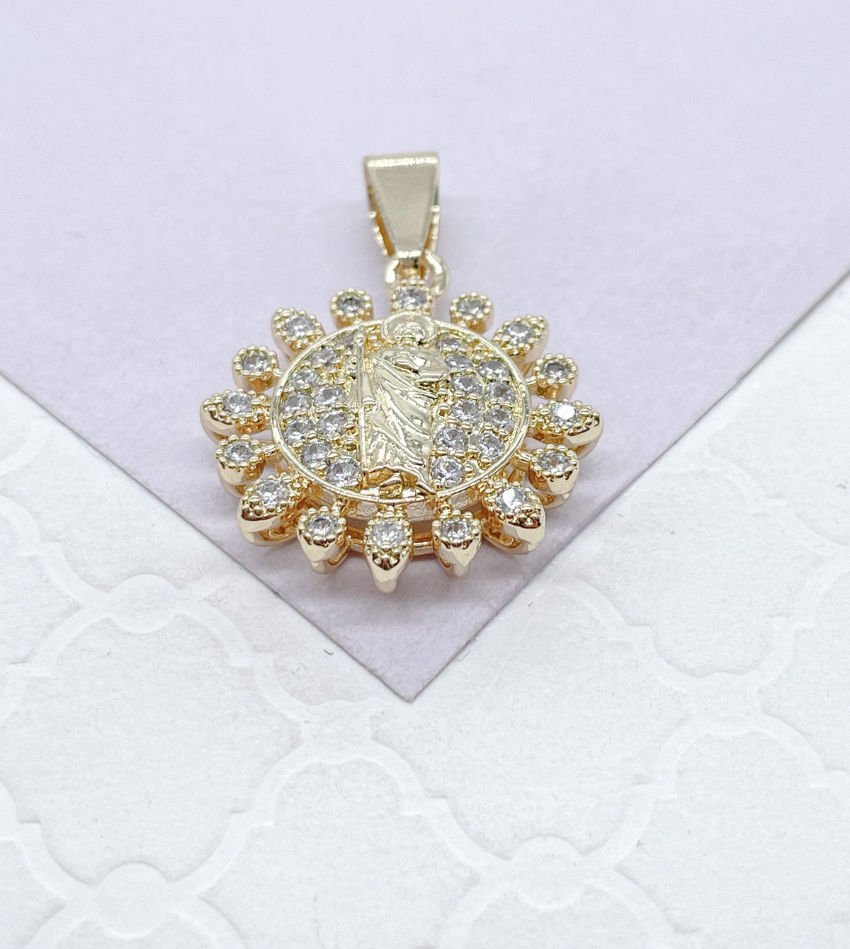 May include: Gold pendant with a clear crystal halo surrounding a religious figure. The pendant has a loop at the top for attaching to a chain.